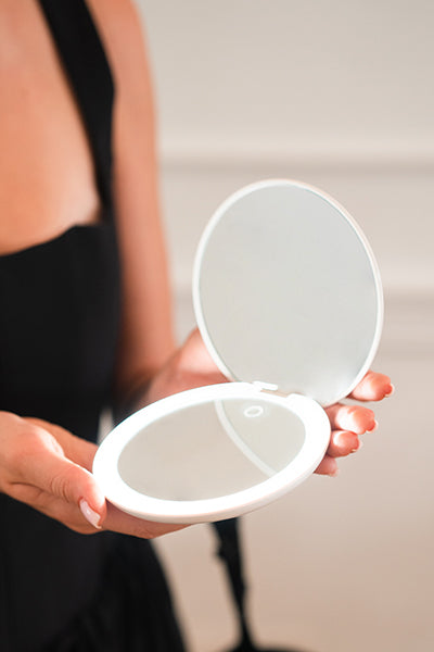 Person holding a white round compact rechargeable makeup mirror with a blurred background