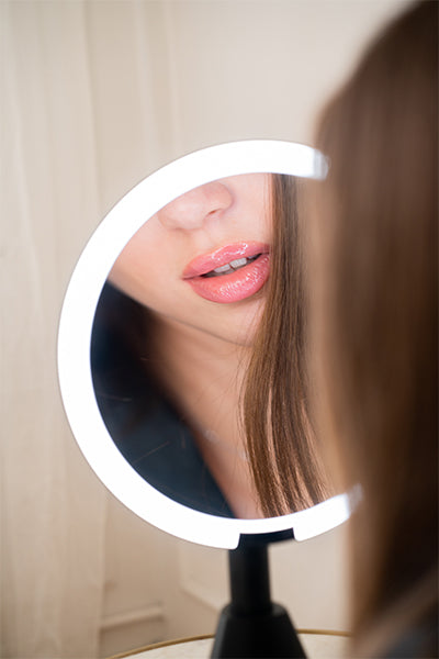 Person using a round rechargeable vanity luxury mirror with LED lights to check their lips.