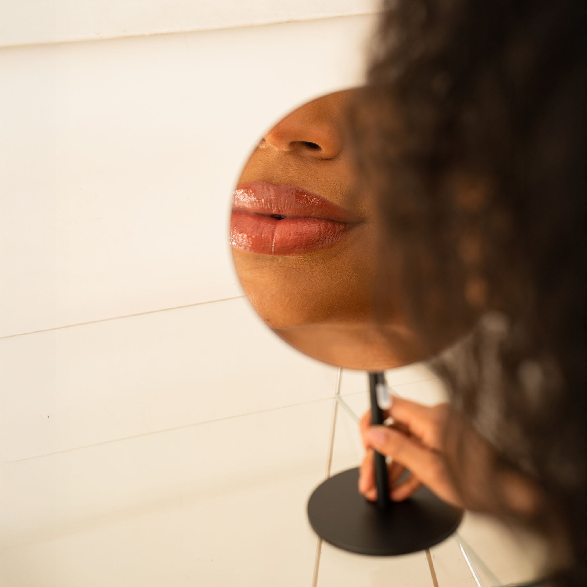 Person holding a round mirror to their face, reflecting their lips._#Silver_Black