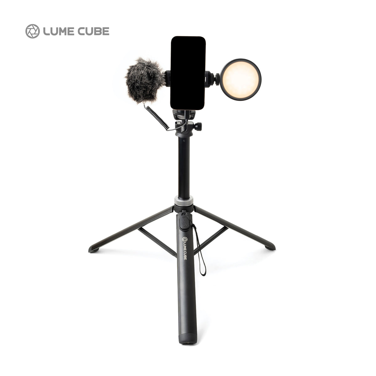 Lume Cube mobile studio light and microphone setup on a tripod, featuring a smartphone in a black clip, a furry wind muff, and a circular ring light, shown on a white background with the Lume Cube logo in the top left.