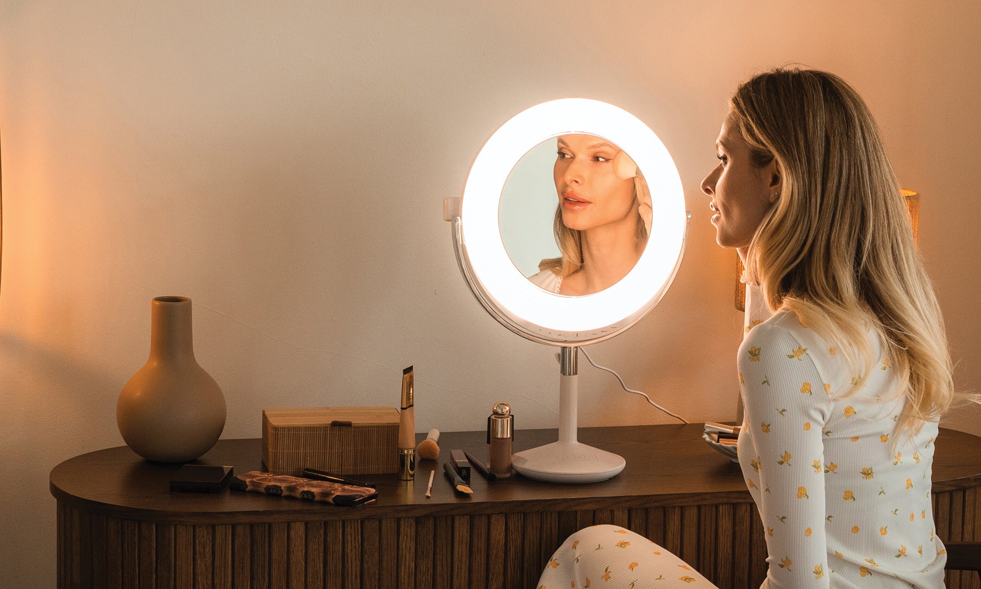 Woman using a round vanity mirror with a light ring in a home setting.