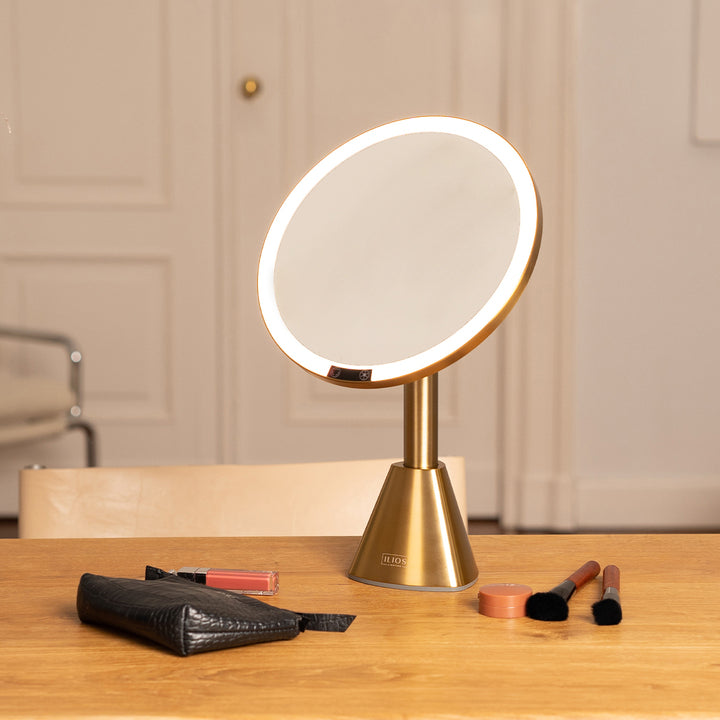 Gold vanity mirror with LED lights on a wooden surface with makeup items.