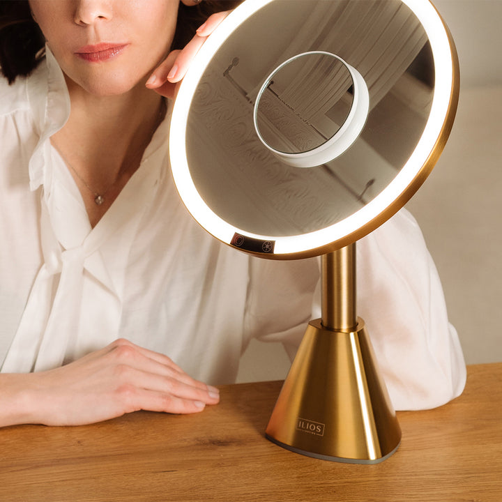 Woman using a gold illuminated 5x zoom makeup mirror with a 10x zoom small mirror on a wooden surface