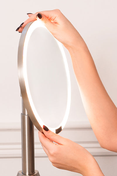 Person holding a modern lighted makeup mirror set mirror with a metallic frame against a neutral background