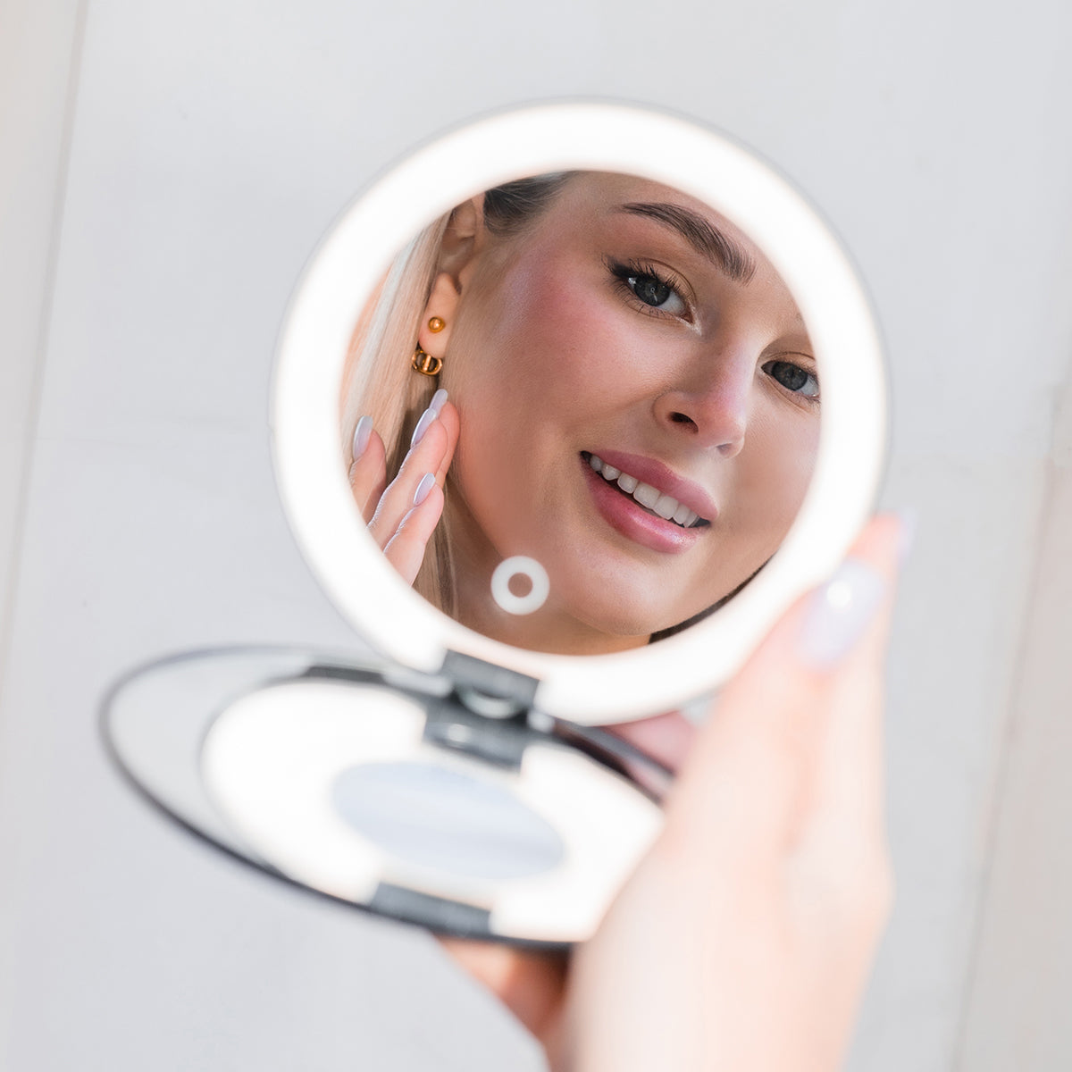 Person holding a round makeup travel makeup mirror with a lighted surface