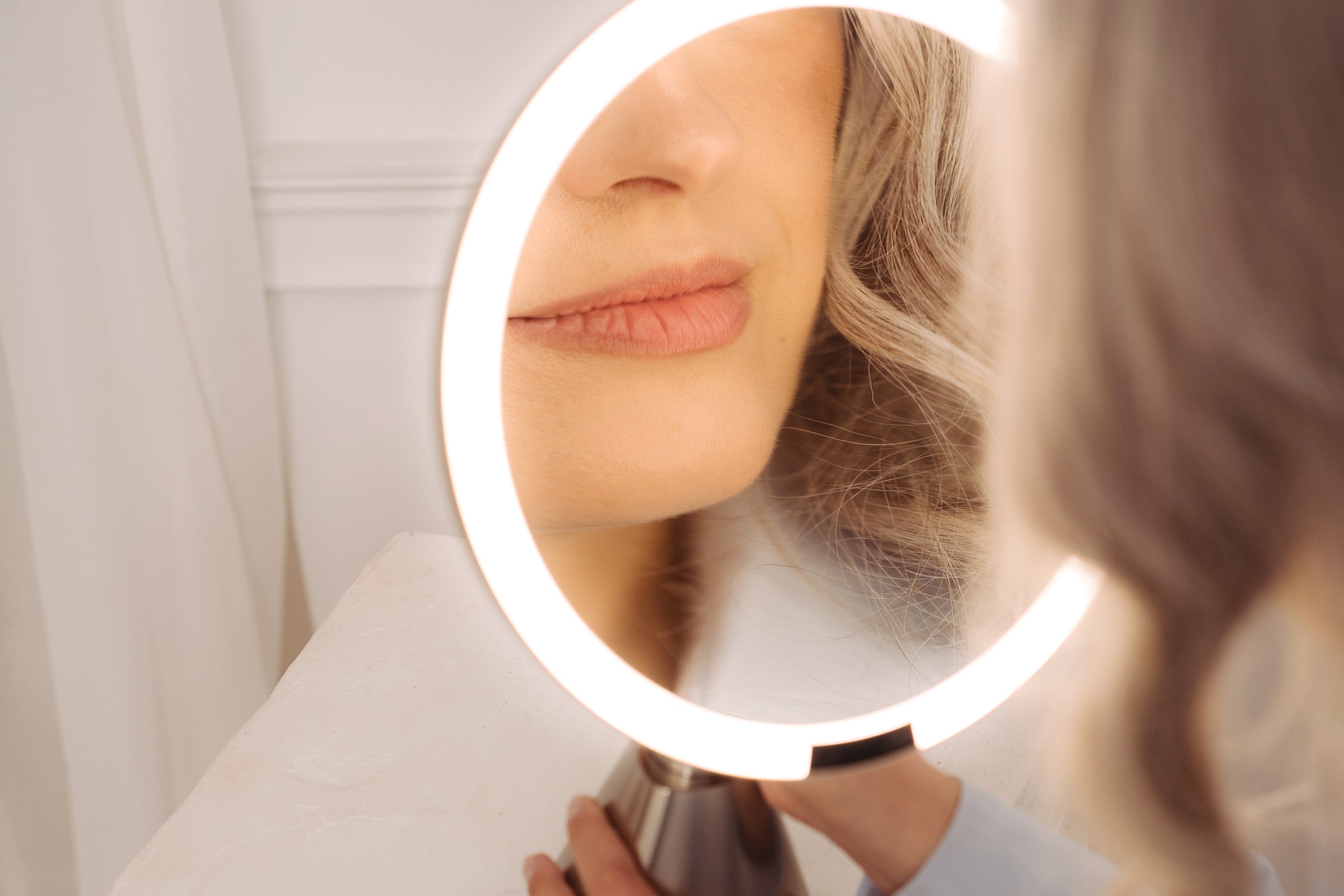 Person using a round, illuminated makeup mirror.