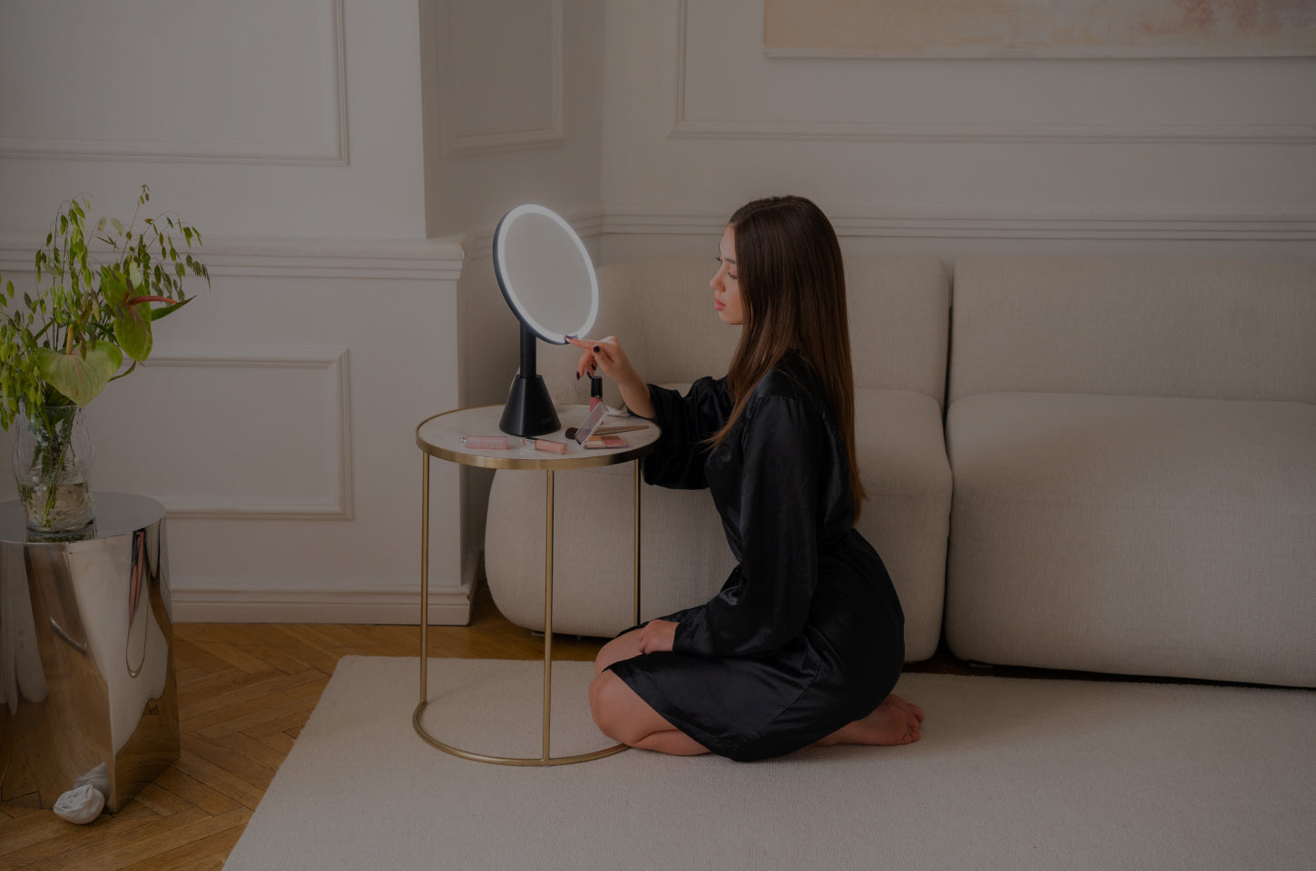 Woman sitting on the floor using a vanity mirror set mirror in a room with a couch and table.